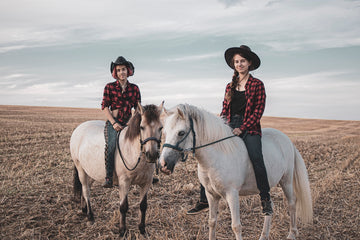 woman in red and white plaid dress shirt riding white horse on brown sand during daytime