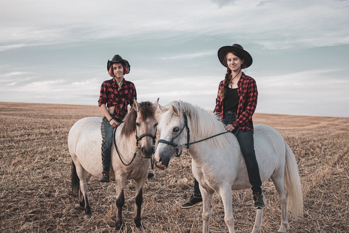 woman in red and white plaid dress shirt riding white horse on brown sand during daytime