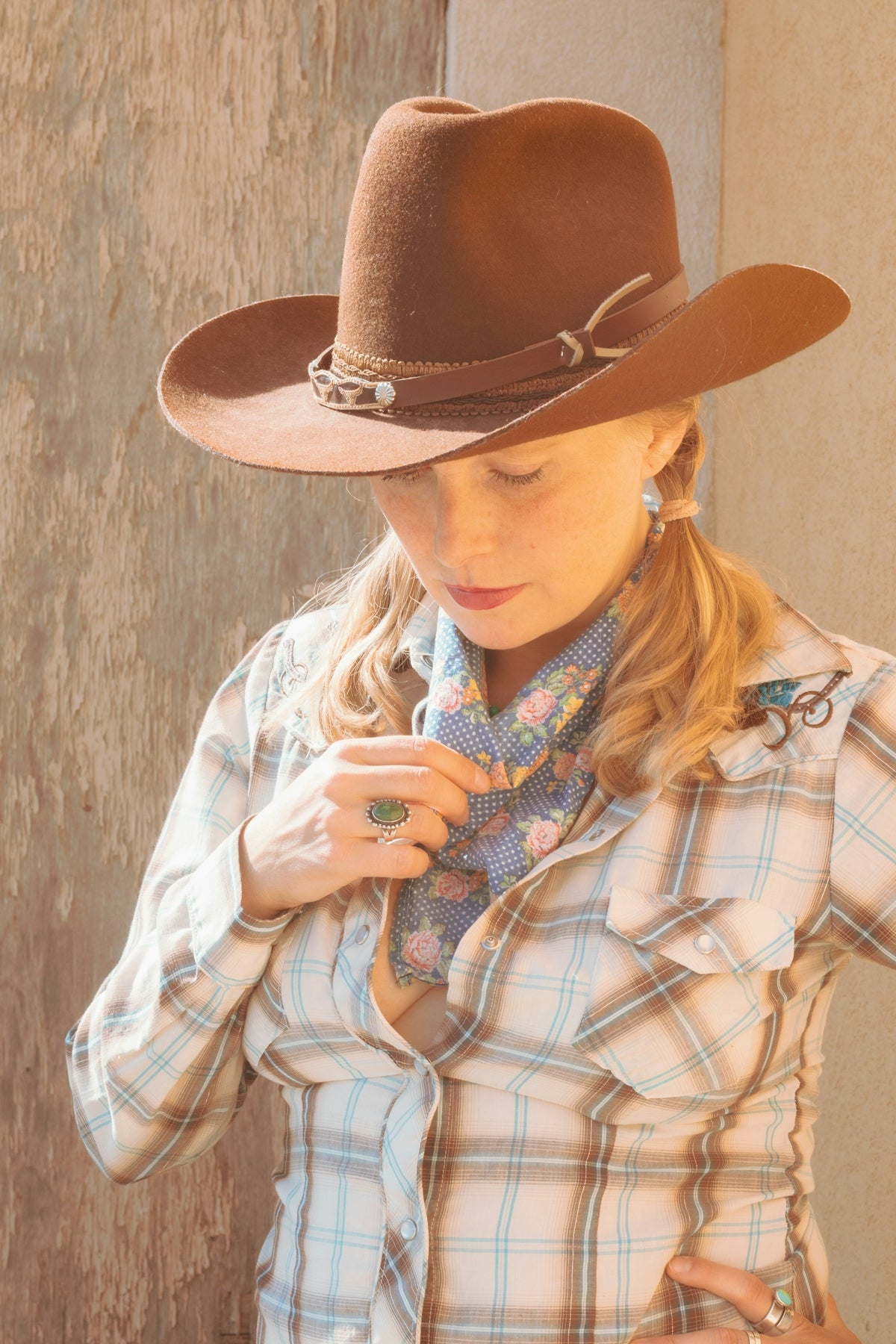 Cowgirl adjusting her scarf while wearing a hat.