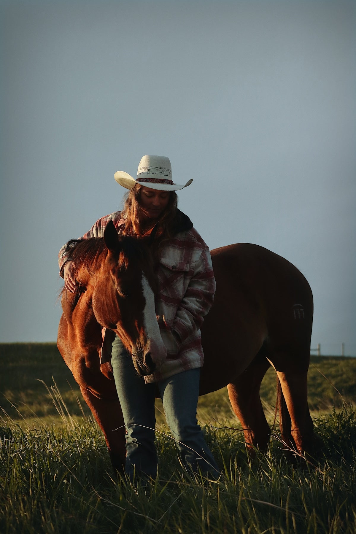 A cowgirl embraces her horse in a field.
