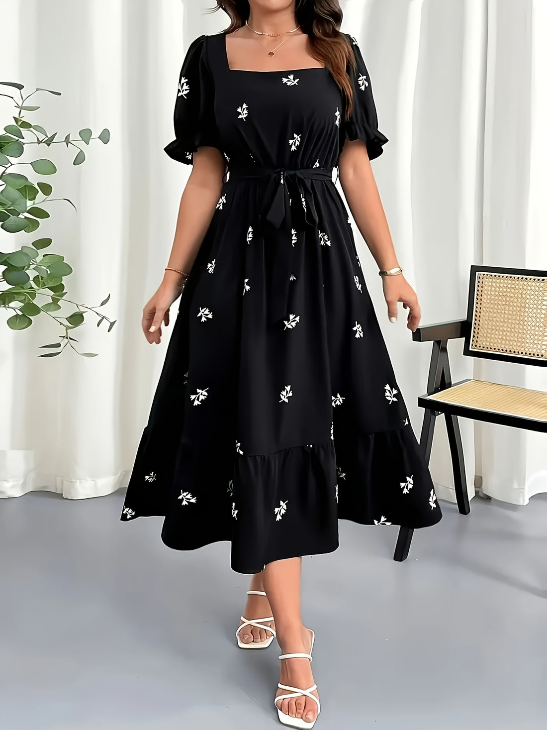 Woman wearing a black dress with white floral patterns in a minimal indoor setting.