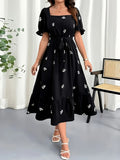 Woman wearing a black dress with white floral patterns in a minimal indoor setting.