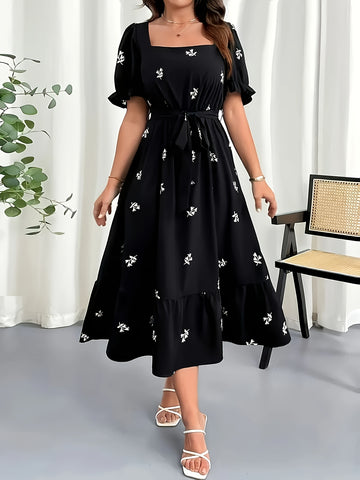Woman wearing a black dress with white floral patterns in a minimal indoor setting.